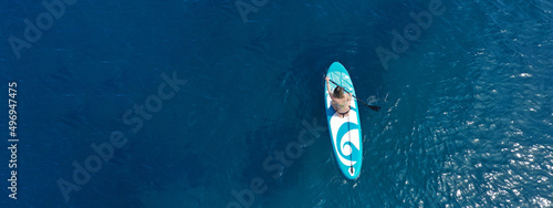 Aerial drone ultra wide panoramic photo with copy space of fit unidentified woman paddling on a SUP board or Stand Up Paddle board in deep blue sea