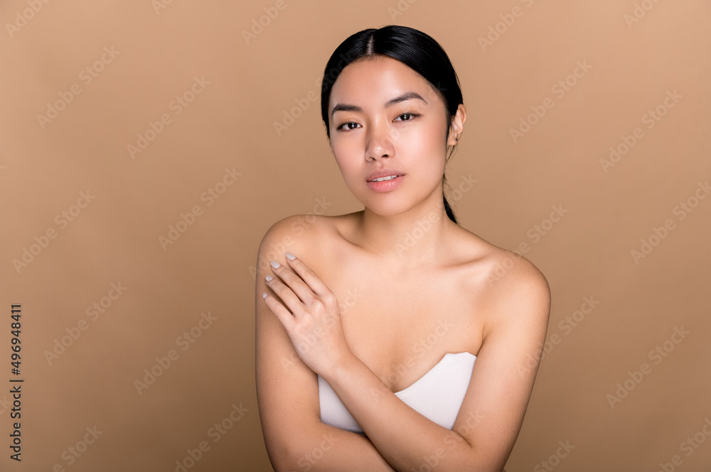 Portrait of a lovely attractive well-groomed brunette Chinese girl, with clean healthy perfect skin, posing over an isolated beige background, smiling. Beauty and care concept Portrait of a lovely attractive well-groomed brunette Chinese girl, with clean healthy perfect skin, posing over an isolated beige background, smiling. Beauty and care concept