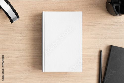 White book mockup with workspace accessories on the wooden table.