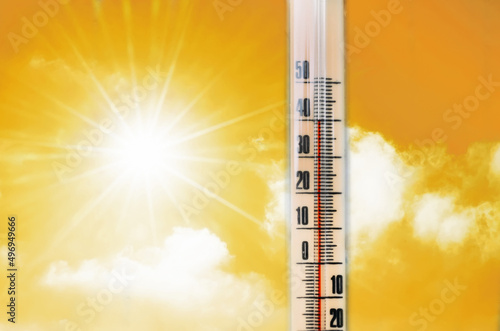 Thermometer against the background of an orange yellow hot glow of clouds and sun, concept of hot weather. Above 40 degrees Celsius.