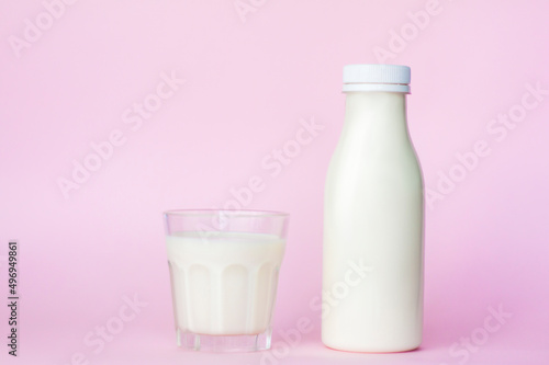 A bottle and a glass of white milk, highlighted on a pink background, close-up.