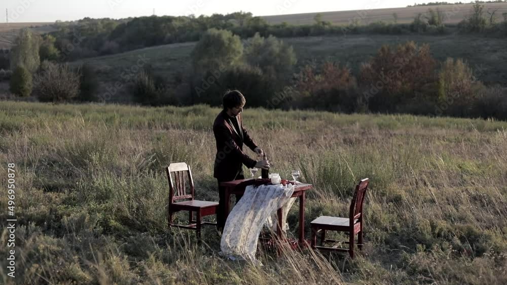 A man pours wine into glasses, a wooden table in an open field. A man pours wine into glasses, a wooden table in an open field.