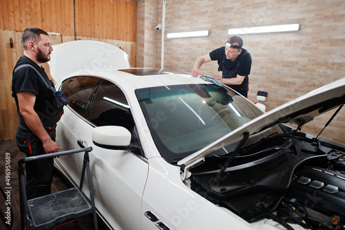 Worker in detailing garage put polyurethane anti-gravel film cover in white luxury car. © AS Photo Family