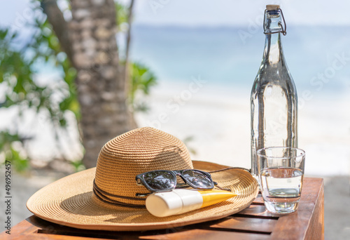 Fototapeta Naklejka Na Ścianę i Meble -  Glass bottle of water, straw hat, sun glasses and sunscreen on the background of the beach in the Maldives