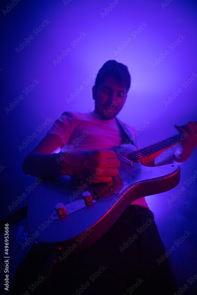 Obraz premium jeune homme qui joue de la guitare électrique en concert, dans une ambiance rock avec des lumières et de la fumée. Il prend du plaisir à jouer du rock et du blues.