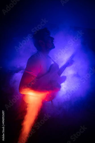 jeune homme qui joue de la guitare électrique en concert, dans une ambiance rock avec des lumières et de la fumée. Il prend du plaisir à jouer du rock et du blues. © Tof - Photographie