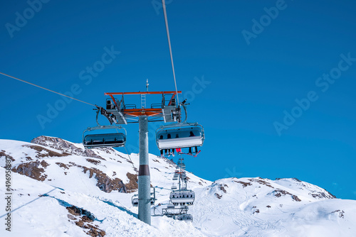 Cable cars traveling over snow covered mountain slope against clear blue sky