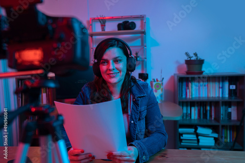 Beautiful Hispanic woman in front of a video camera recording a blog in her studio with red and blue lights inside her house
