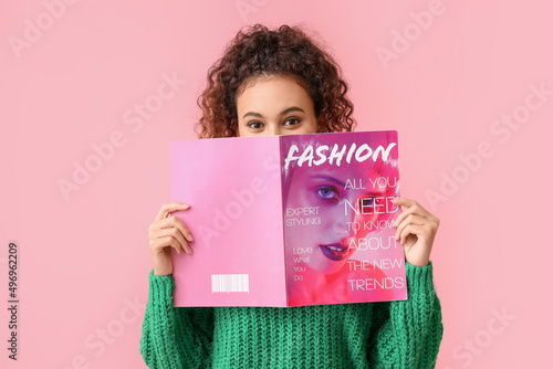 Young African-American woman in green sweater reading magazine on pink background