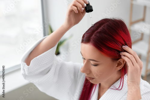 Beautiful young woman using serum for hair growth at home