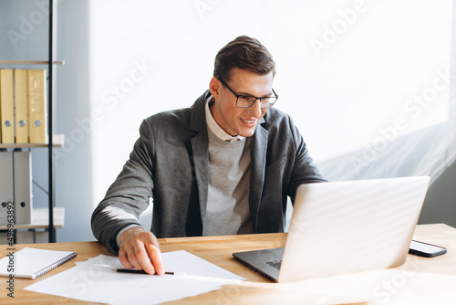 Modern smiling man, office worker working on laptop