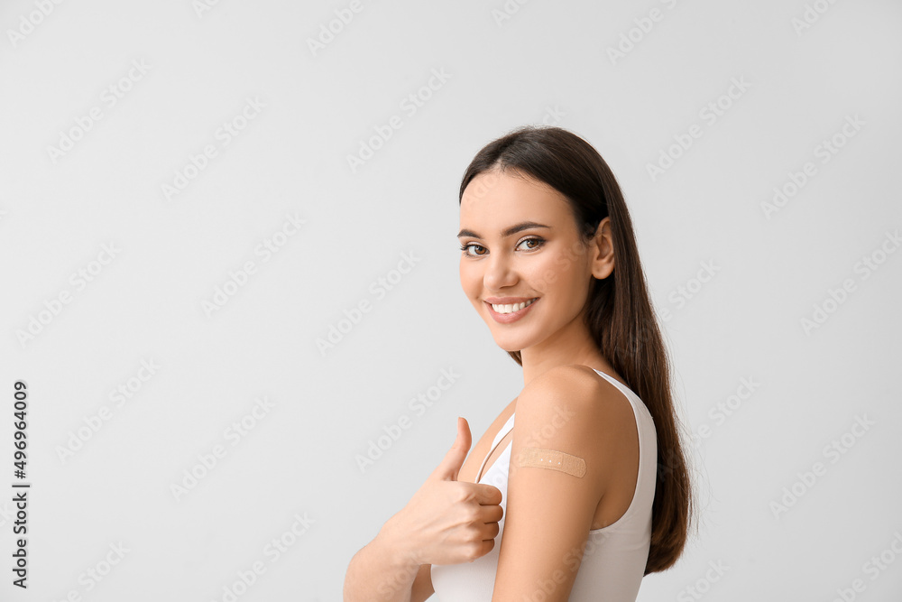 Young woman with applied medical patch showing thumb-up on light background Young woman with applied medical patch showing thumb-up on light background