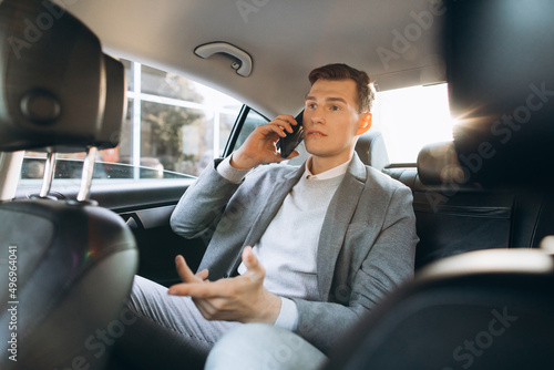 Young businessman talking on a mobile phone while sitting in the back seat of a car. © anatoliycherkas