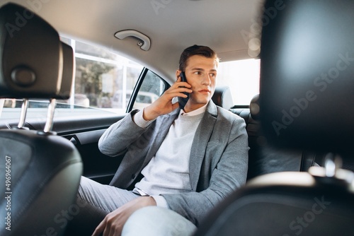Young businessman talking on a mobile phone while sitting in the back seat of a car.
