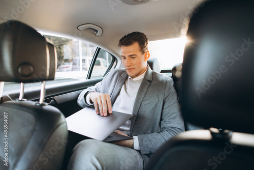 A modern businessman using a laptop computer while sitting in the back seat of a car.