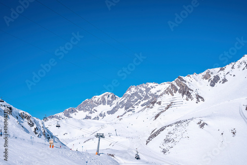 Ski lift moving over snowy mountain. Chairlift on beautiful white landscape against clear blue sky. Scenic view of alps in winter.