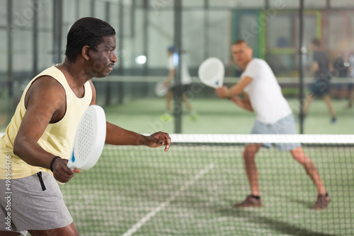 Focused African American playing friendly paddleball match on small closed court. Concept of concentration in competition.
