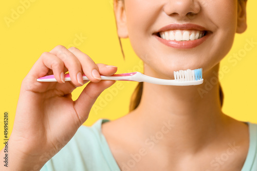 Smiling young woman with tooth brush on yellow background  closeup