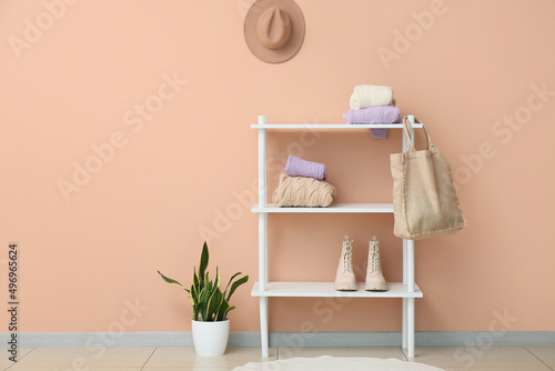 Shelving unit with knitted sweaters  shopping bag and shoes near beige wall