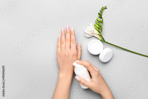 Woman with beautiful manicure applying cream on grey background