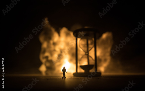 Time concept. Silhouette of Hourglass clock and old vintage wood clock with arrow and smoke on dark background with hot yellow orange red blue cold back lighting, or symbols of time with copy space