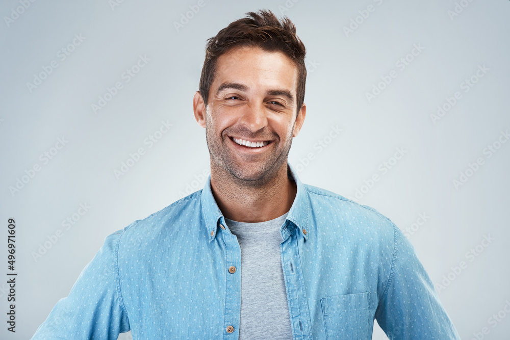 Always a cheerful one. Portrait of a cheerful young man smiling brightly while standing against a grey background. Always a cheerful one. Portrait of a cheerful young man smiling brightly while standing against a grey background.