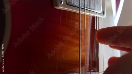 Fingers picking the strings of a Les Paul electric guitar in cherry sunburst. Static close up shot photo