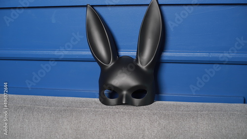 Máscara de conejo de cuero negro fetiche para jugar rol sobre un sofa de la sala junto a la pared azul photo