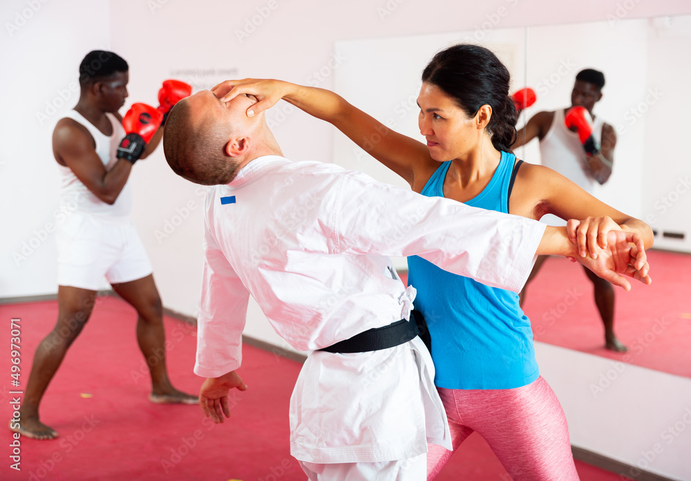 Oriental woman training self-defence moves with her trainer. African-american man standing in fighting stance and boxing in front of mirror.