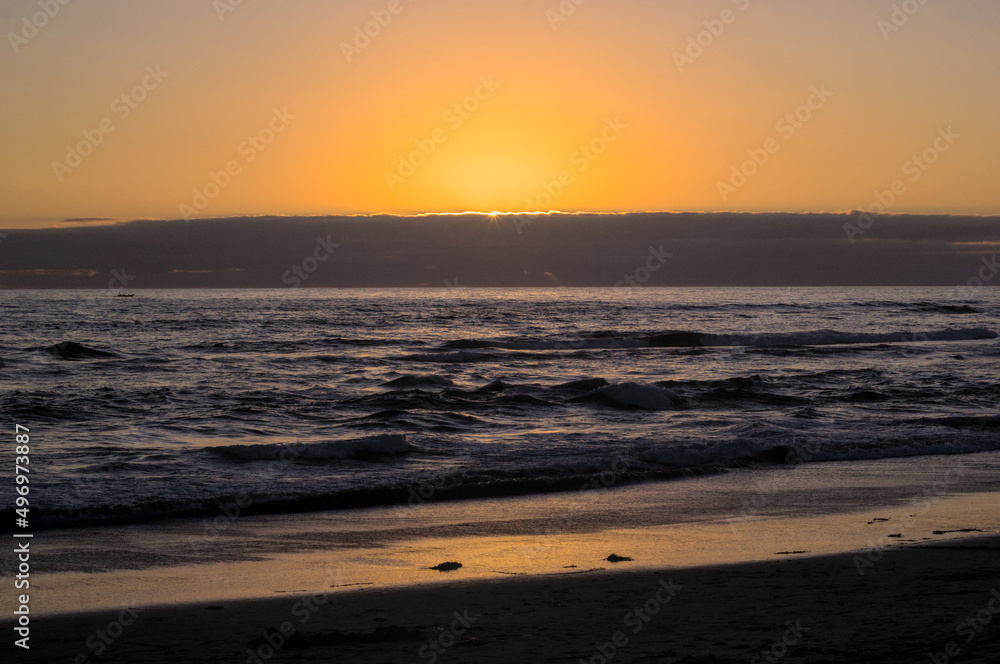 puesta de sol y ocaso en la orilla de playa con nubes en el horizonte y un pequeño bote