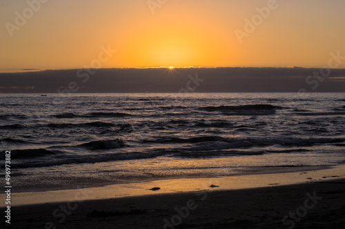 puesta de sol y ocaso en la orilla de playa con nubes en el horizonte y un pequeño bote