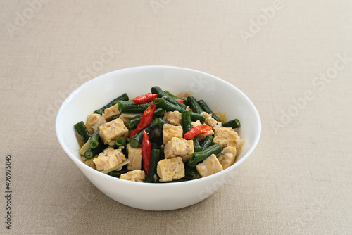 Oseng tempe kacang panjang or stir fried tempeh and long bean, Indonesia traditional cuisine, served on white bowl. Selected focus.
