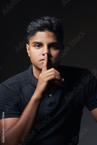 Silence is the best answer. Studio shot of a young man posing with his finger on his lips.