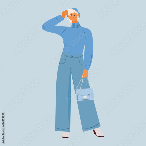 A girl with blond hair and a short haircut is dressed in a turtleneck and jeans. In the hands of a bag. Fashion clothes. Blue colors. Girl model posing for a photo.