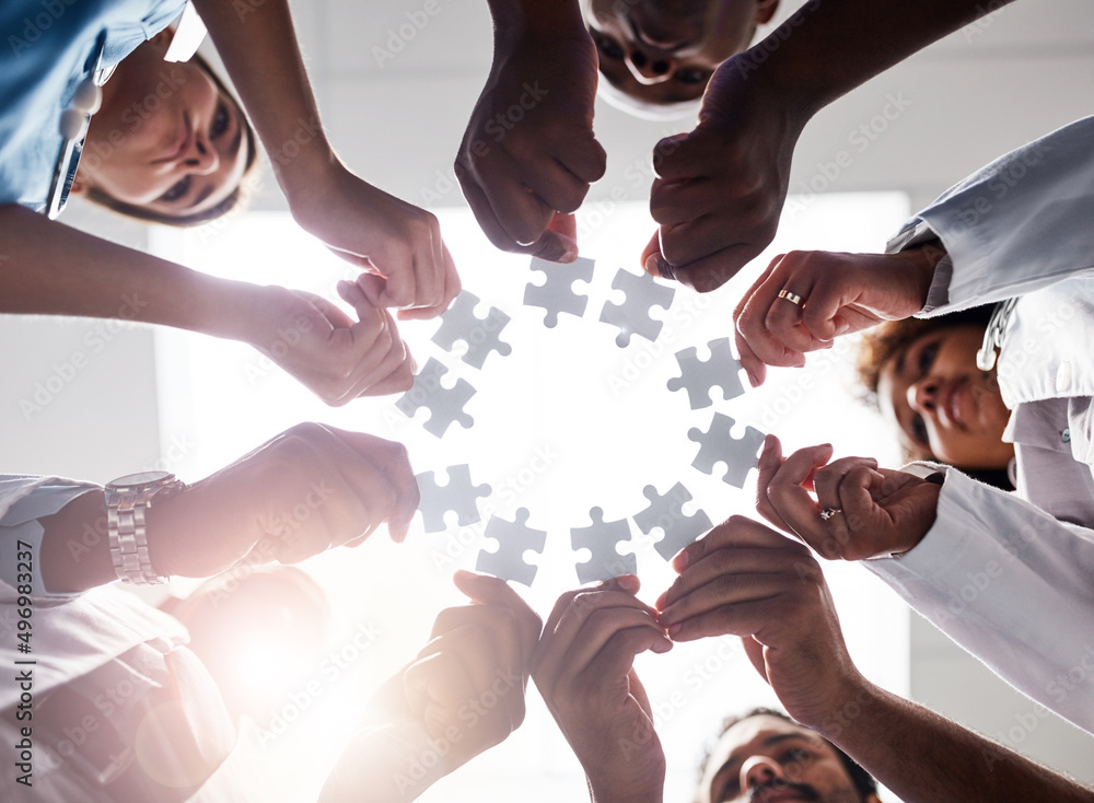 Obraz premium Everyone plays their part here. Low angle shot of a group of doctors forming a huddle while each holds a puzzle piece inside of a hospital.