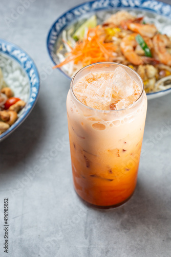 A view of a glass of Thai tea, with a few Thai entrees in the background.