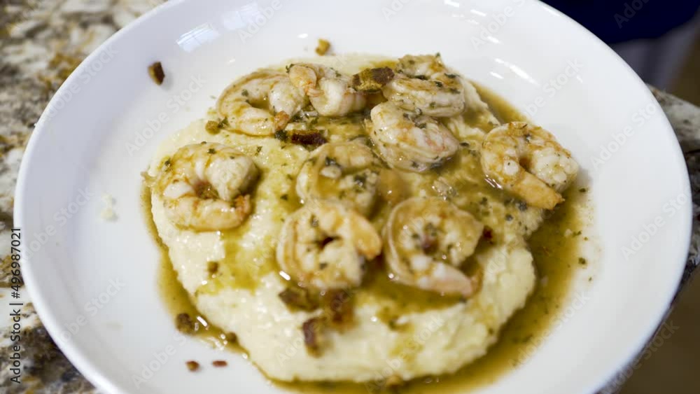 Sprinkling chopped bacon on a plate of shrimp and grits Sprinkling chopped bacon on a plate of shrimp and grits