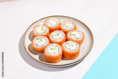 Philadelphia maki roll on ceramic plate with chopsticks. Salmon sushi roll with philadelphia cheese on coloured background. Japanese menu concept. Salmon sushi roll in modern style.