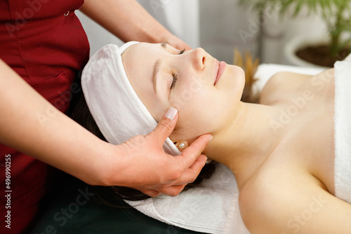 Close up photo of a amazing young woman face with closed eyes undergoing face massage procedure in spa salon, face care concept.