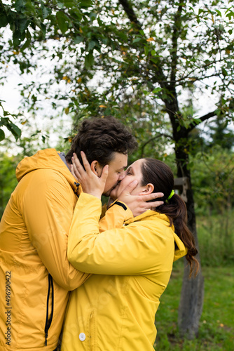 A married couple in yellow raincoats in the rain in their backyard. Front view. © Anastasiia