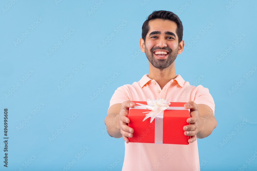 Young man looking at camera with smile and showing gift Young man looking at camera with smile and showing gift