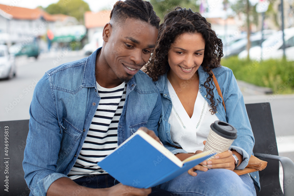 Obraz premium young couple on bench smiling and reading book together