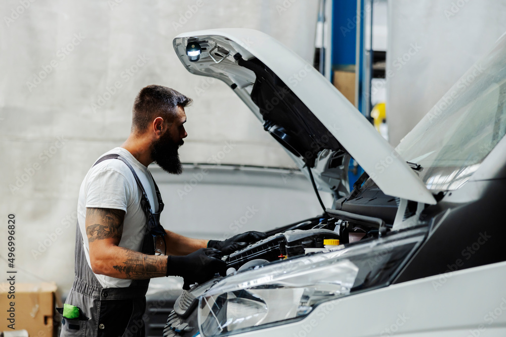 An auto-mechanic fixing engine on vehicle at workshop. An auto-mechanic fixing engine on vehicle at workshop.