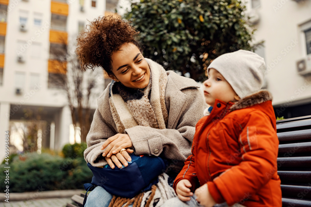 Fototapeta premium A happy young woman, caregiver or nanny, on a bench listening to the little boy talking.