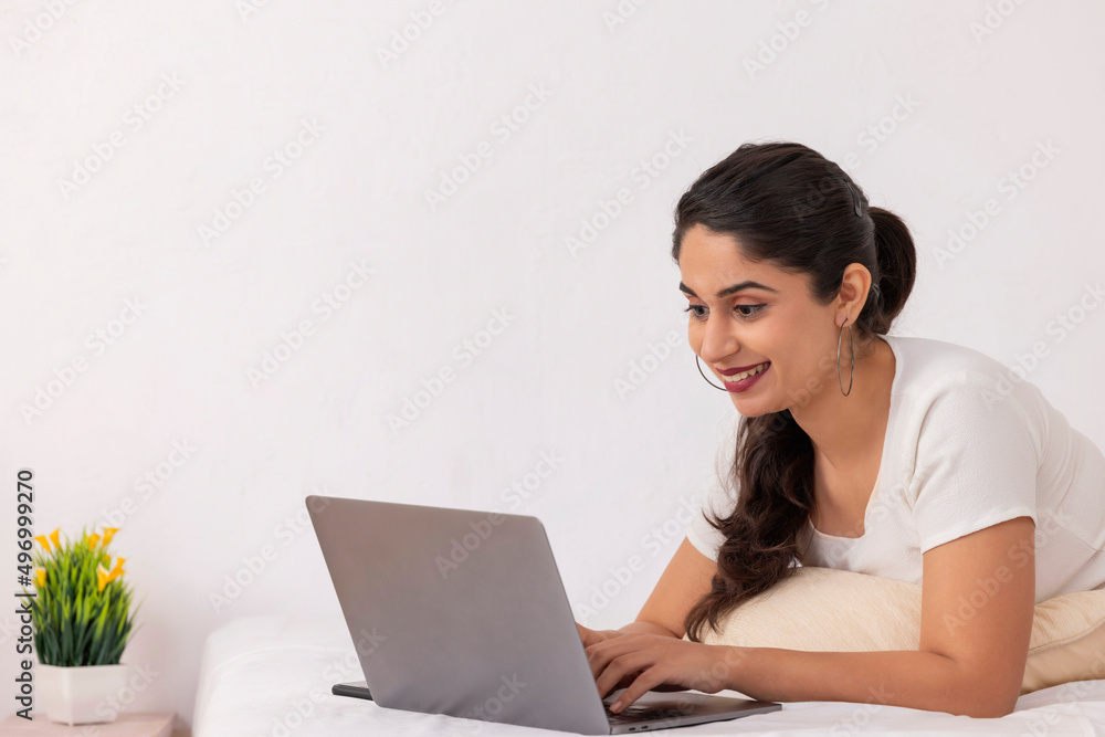 Portrait of young woman using laptop while lying down on bed at home Portrait of young woman using laptop while lying down on bed at home