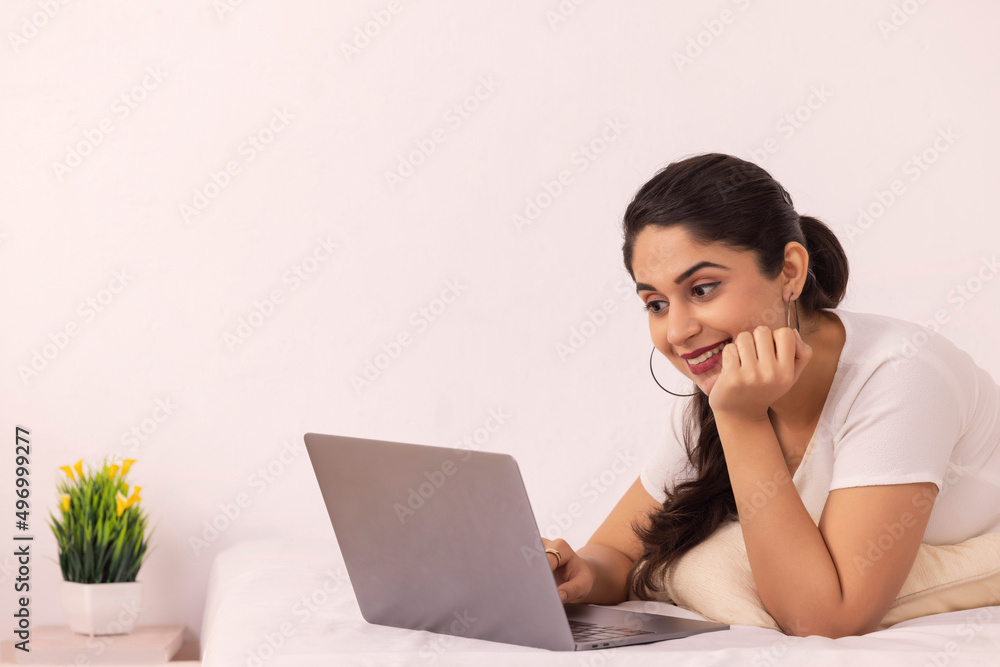 Portrait of young woman using laptop while lying down on bed at home Portrait of young woman using laptop while lying down on bed at home