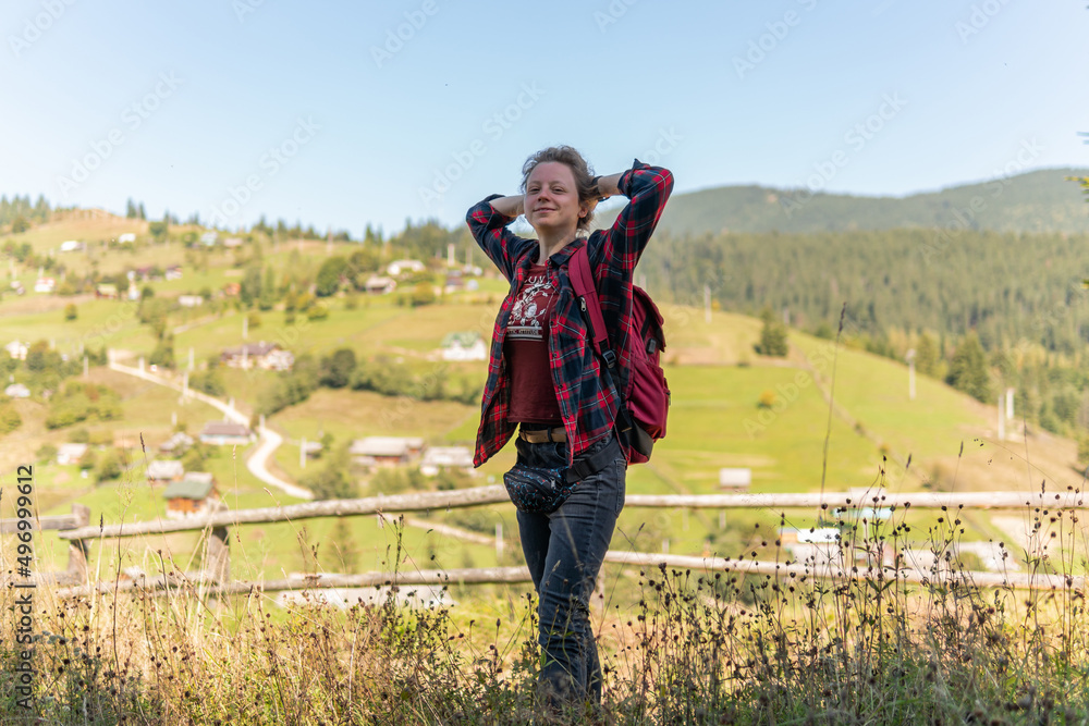 A happy tourist is standing in a shade and smiling in the mountains, near a small village