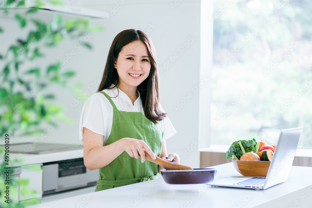 パソコンを見ながら料理する女性（笑顔・カメラ目線）
