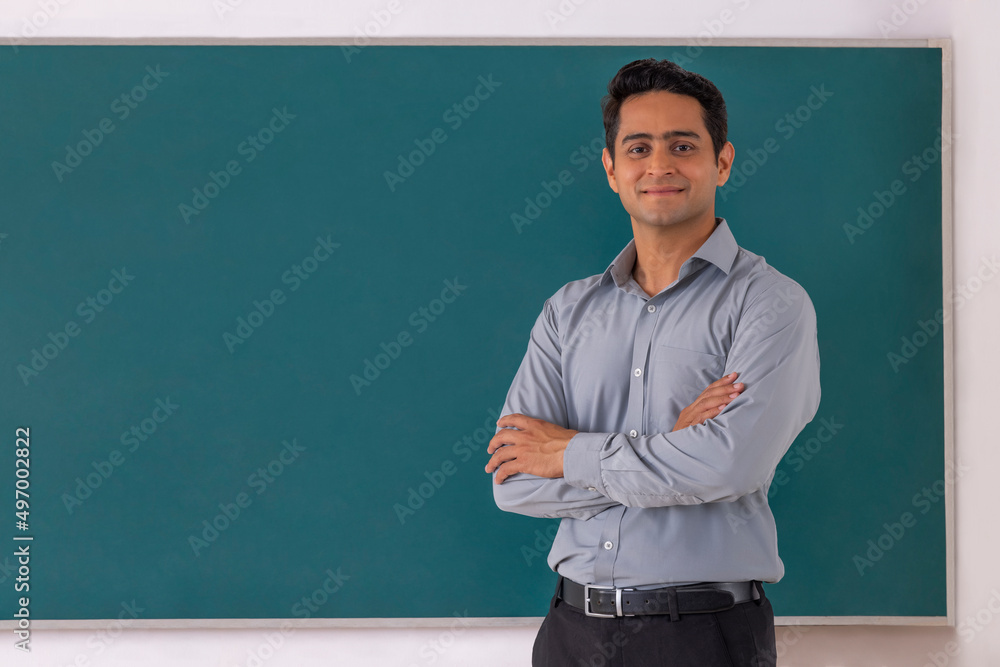 School teacher standing in front of blackboard with arms folded in classroom