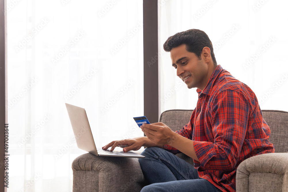 Portrait of a young man shopping online through laptop using credit card Portrait of a young man shopping online through laptop using credit card